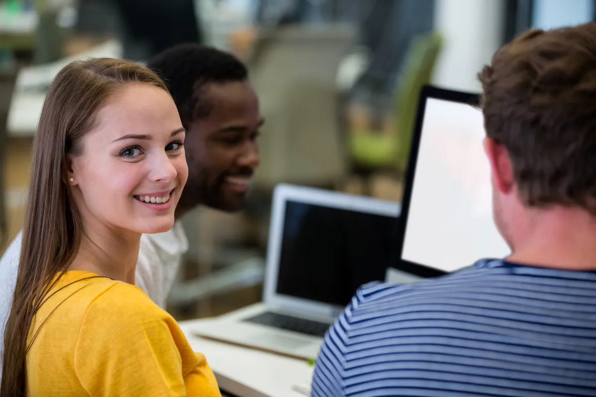 Une jeune professionnelle souriante travaille avec ses collègues dans un bureau lumineux.